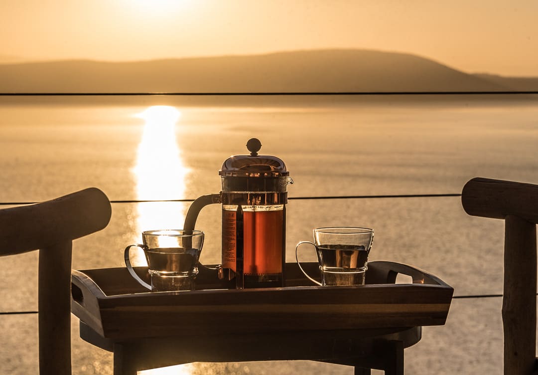 A coffee set laid out on a table as the sun rises over water