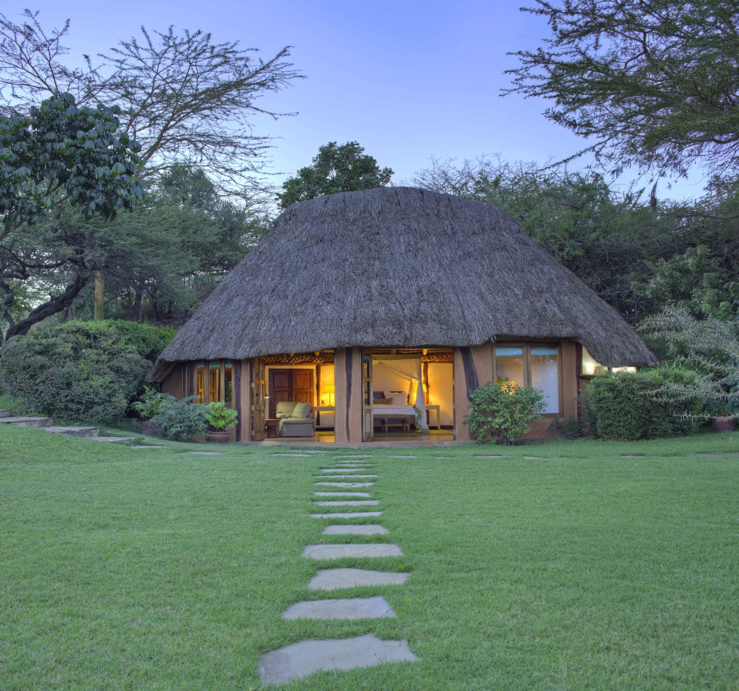 A thatched cottage lit from within at dusk, stepping stones across the lawn