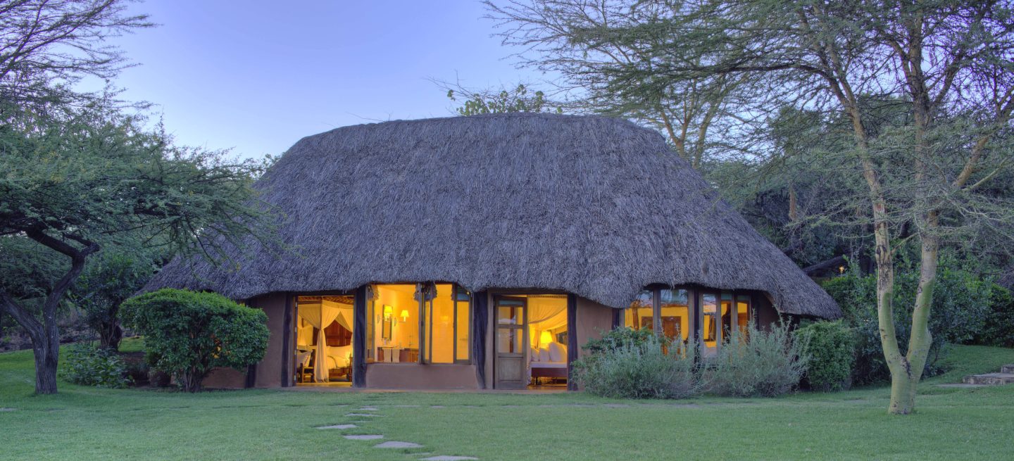 A family cottage lit at dusk with lawn running up to the veranda