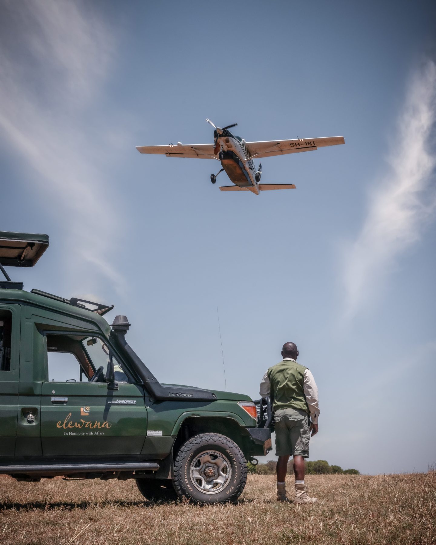 A light aircraft passing low over a safari vehicle and its guide