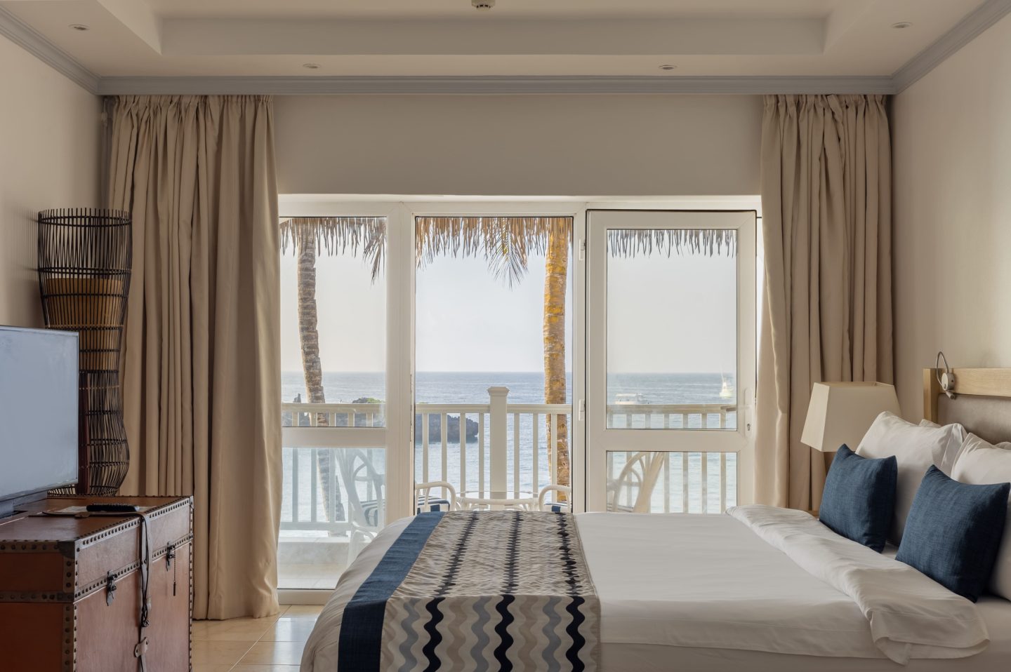 A bedroom with balcony doors standing open to the sea