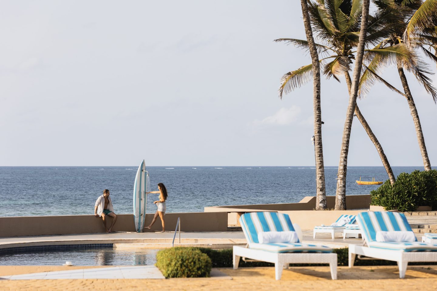 A pool edged with loungers and palms, the ocean just beyond