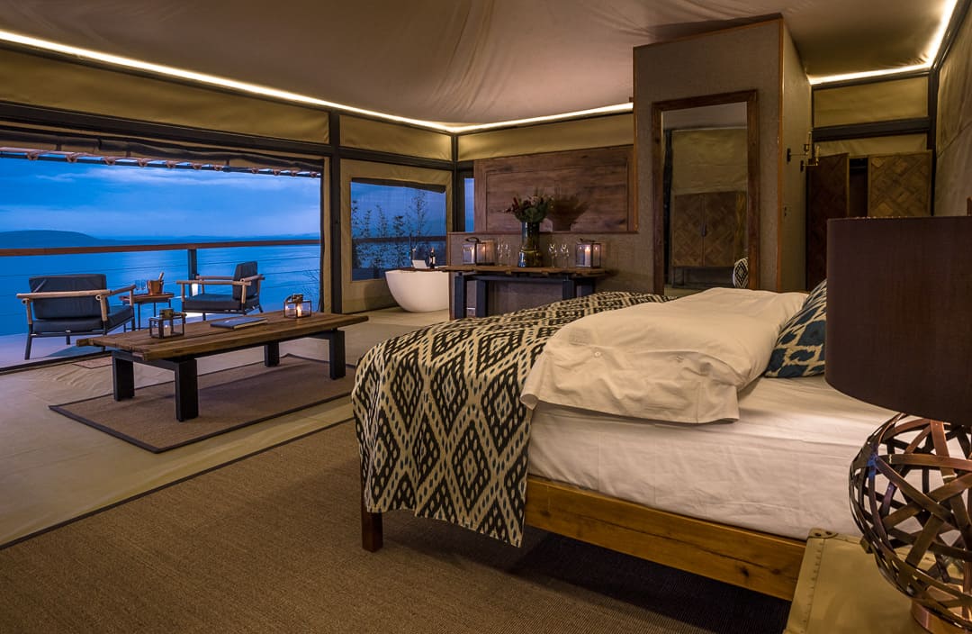 A tented bedroom with the bed facing open doors and the sea beyond
