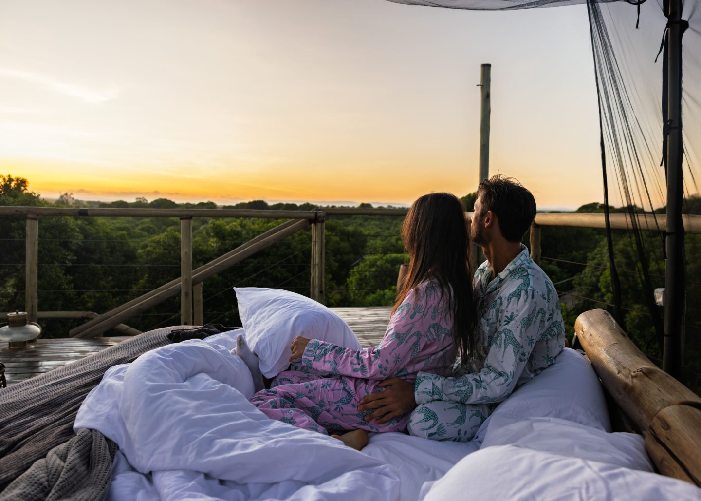Two guests in bed under a mosquito net, looking out at sunrise
